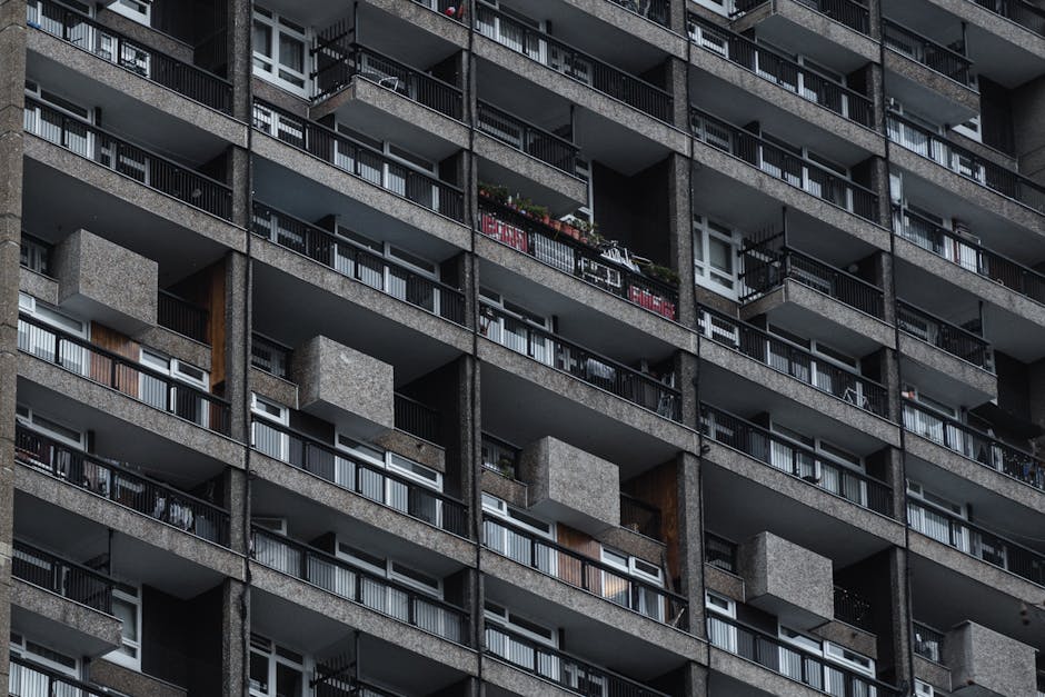 A close-up view of a residential building facade showing multiple floors with balconies and windows. The building features a pink and white exterior with balconies that have metal railings, some of wh